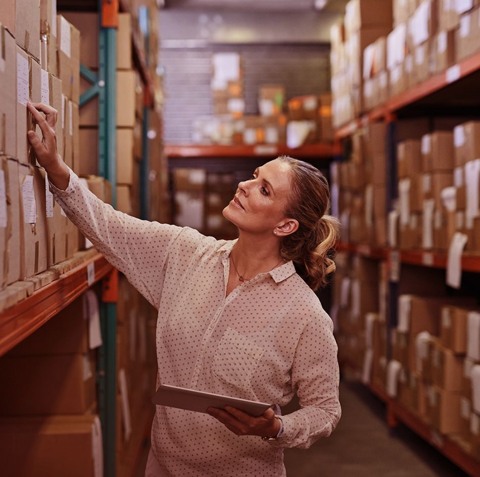Woman working in warehouse with digital tablet checking inventory boxes