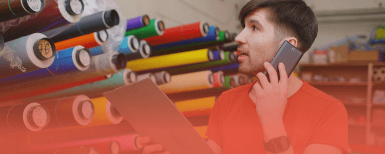 Employee holding a phone and clipboard while checking rolls of material in a warehouse, illustrating manufacturing data challenges for DPP