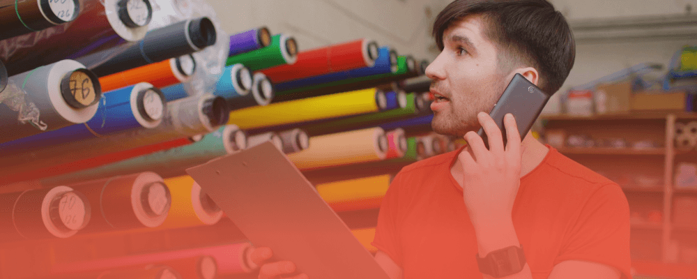Employee holding a phone and clipboard while checking rolls of material in a warehouse, illustrating manufacturing data challenges for DPP