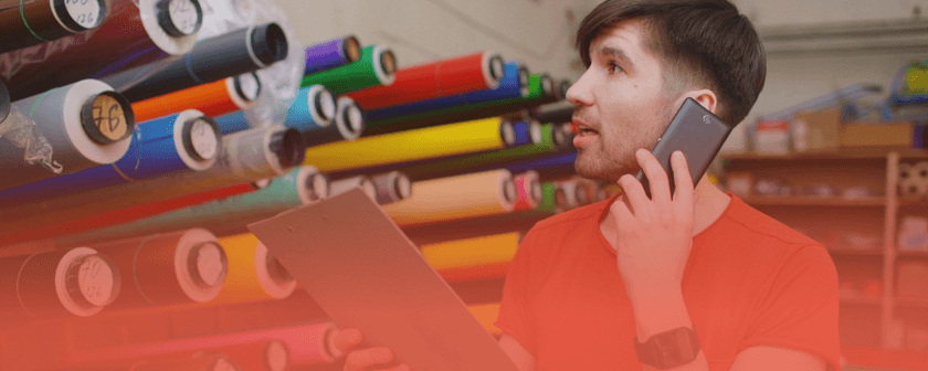 Employee holding a phone and clipboard while checking rolls of material in a warehouse, illustrating manufacturing data challenges for DPP