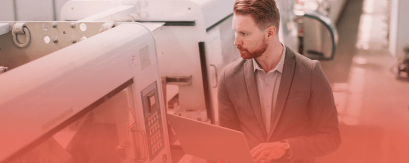 Manufacturing professional using a laptop on the factory floor, illustrating how headless CMS helps solve slow website performance issues for manufacturers.